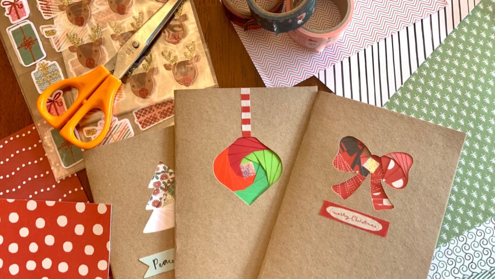 Homemade Christmas cards laying on top of decorative paper, stickers, washi tape, scissors