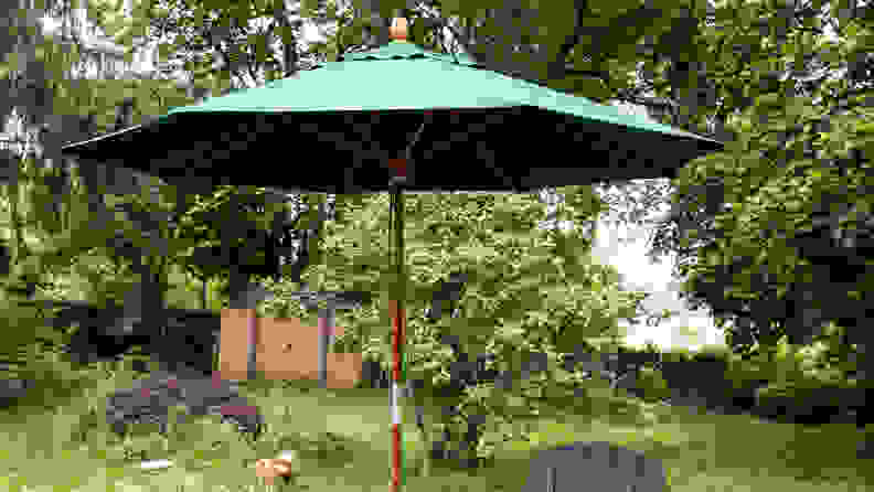 L.L. Bean Market Umbrella with a wooden pole and green fabric umbrella opened in a backyard with grass and trees.