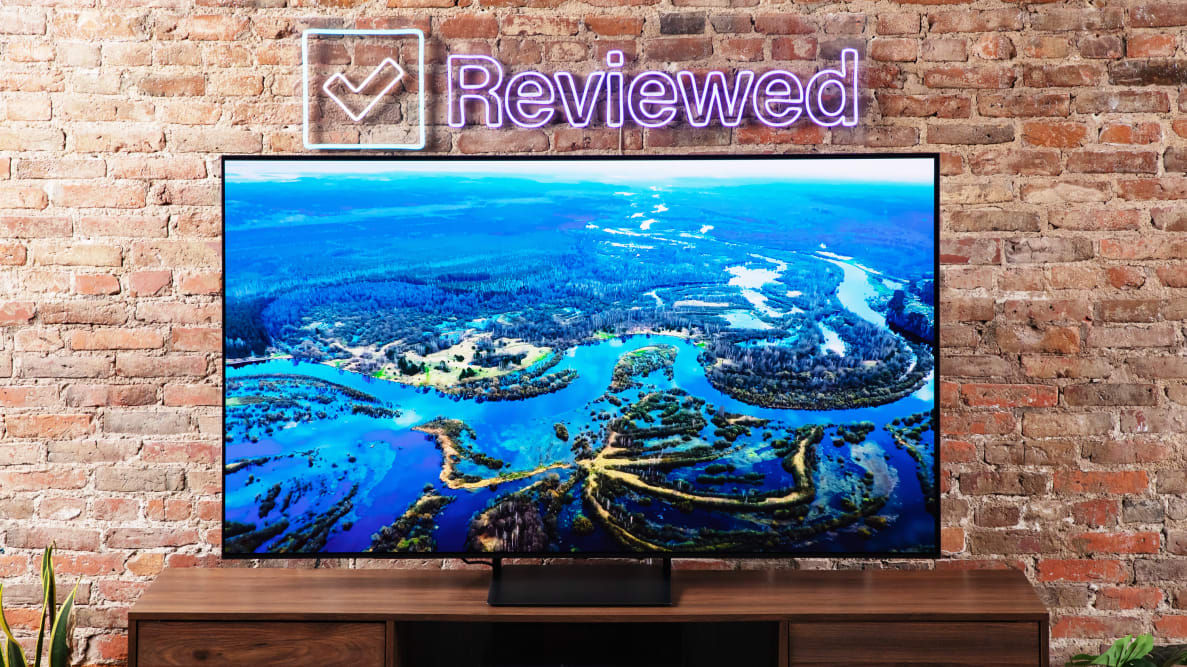 The Samsung S90C QD-OLED TV on an entertainment center with a brick background.