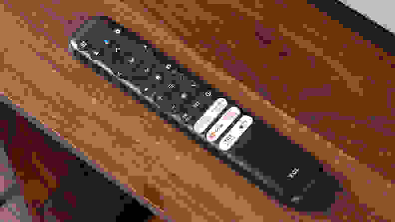 TCL Q6 LED TV remote sitting on top of wooden TV stand.