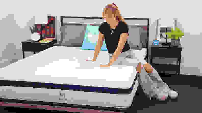 Person sitting on Helix Midnight mattress while using hands to press test the firmness.