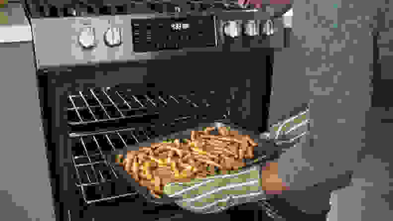 A person removes a tray of air-fired French fries from an oven.
