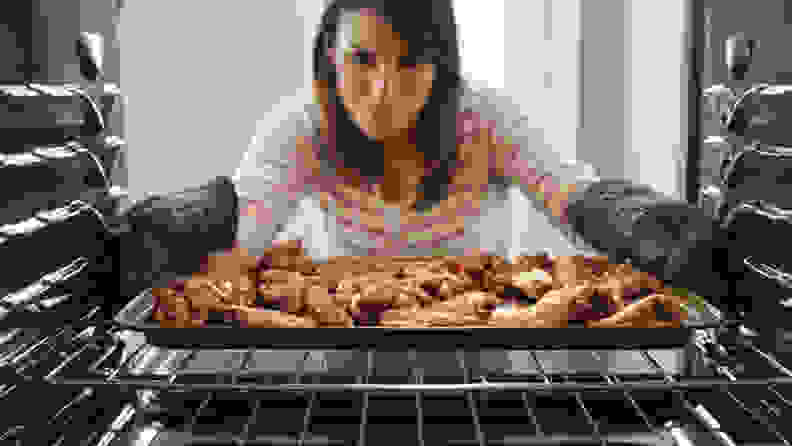 A person removes a tray of chicken wings from an oven.