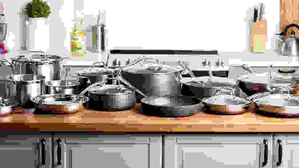 Three complete cookware sets are lined up on a kitchen island