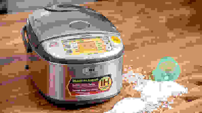 Rice cooker sitting on a table with spilled rice next to it.