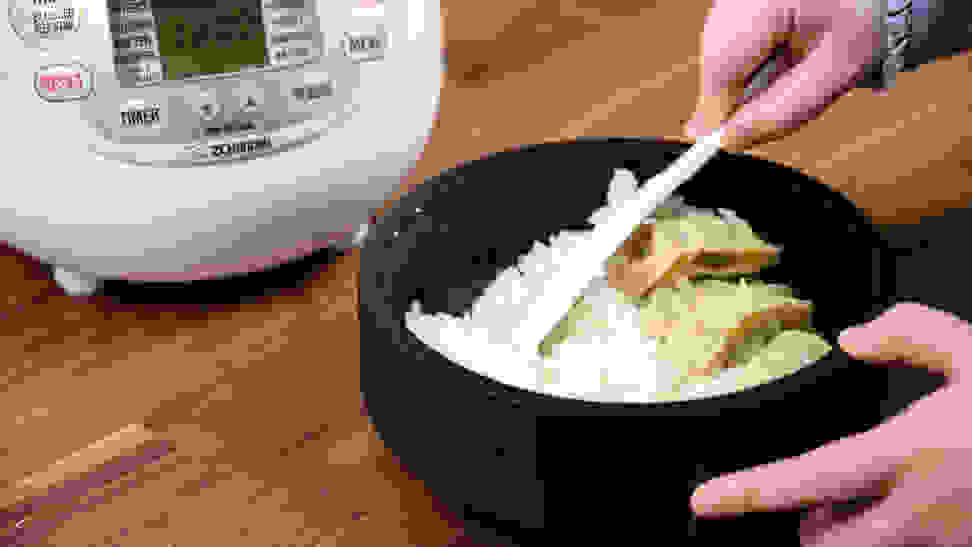Cooked rice in a bowl next to a rice cooker.