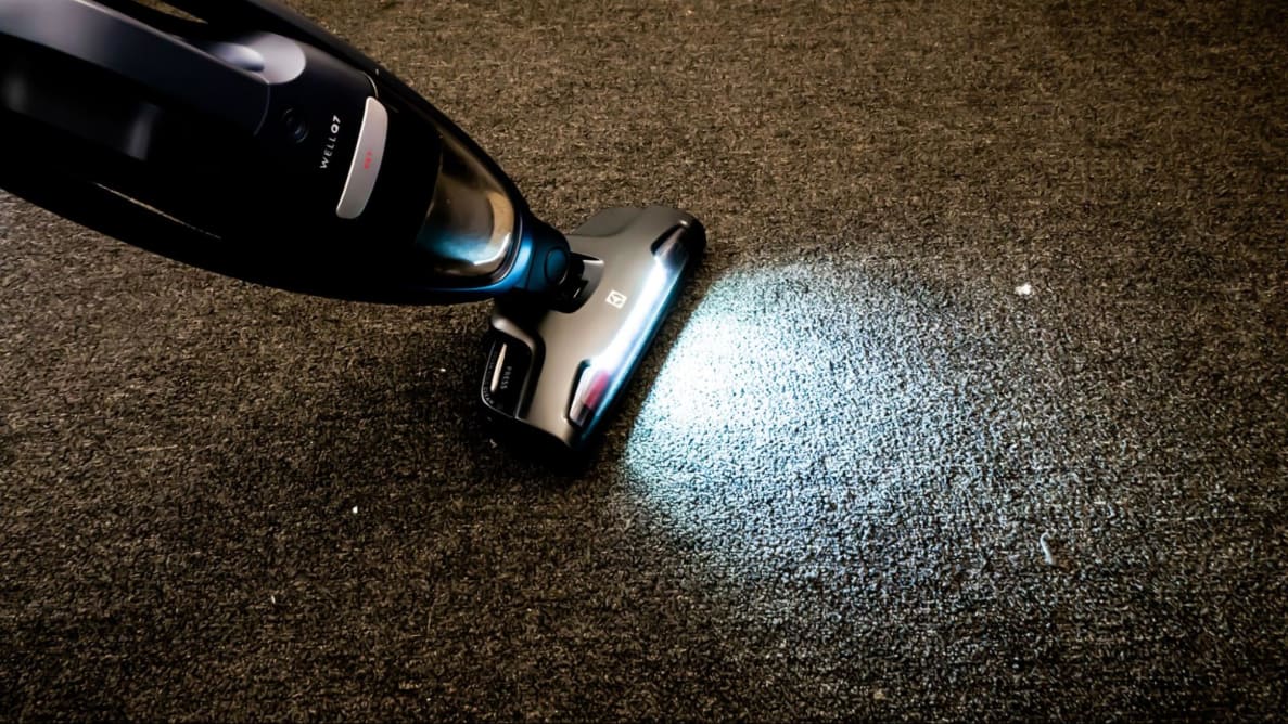 A cordless vacuum on brown carpet with its LED lights on.