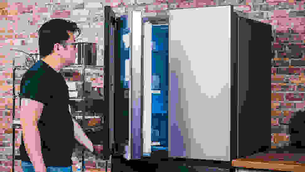 An Asian man opens a door to a stainless steel refrigerator