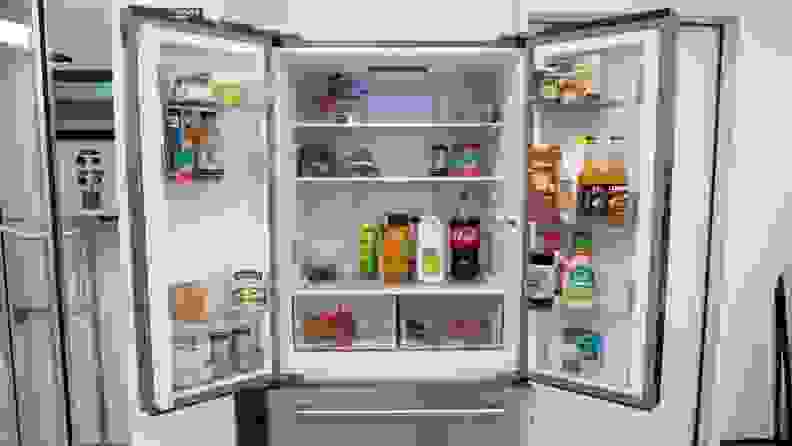 A close-up of the fridge with its top two doors open, revealing an interior stocked with food.