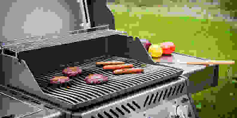 Gas grill open, revealing cooking burgers and hot dogs