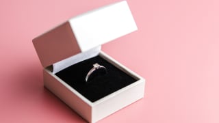 This is an engagement ring in a white box against a pink background.