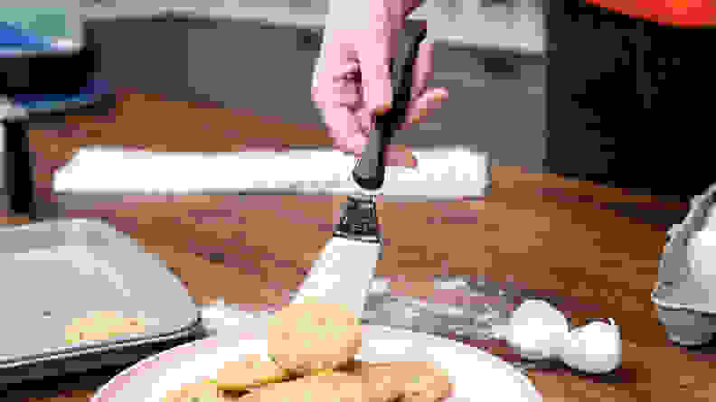 A hand moving a cookie onto a plate with a metal spatula