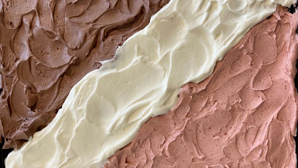 A photo of Neapolitan icing on a sheet cake in the following order from left to right: chocolate, vanilla, and strawberry.