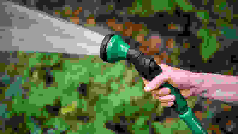 A person sprays water out of a green Dramm hose nozzle.