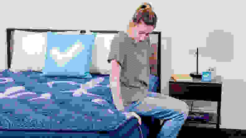 A person sitting on the edge of a mattress.