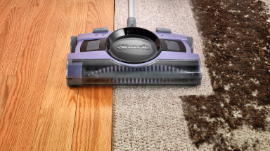 Close-up photo of the Shark V2950 Cordless Sweeper, which is lavender in color, as it cleans a dirty carpet.