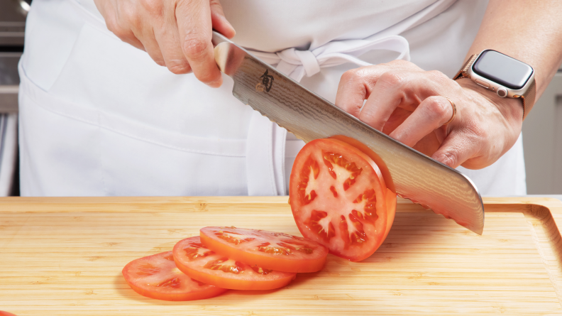 Hand using Shun bread knife to slice into a tomato