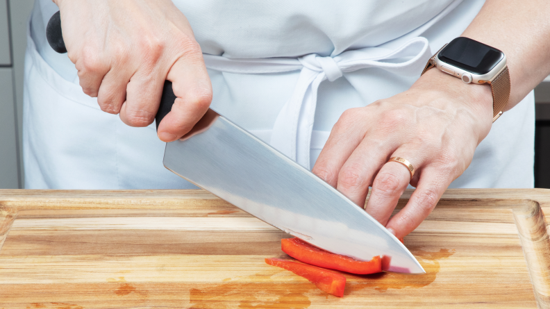 Person slicing red bell pepper on wooden cutting board with Victorinox knife