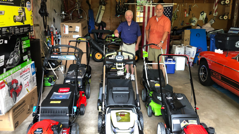 Two testers stand with eight lawn mowers in a garage.